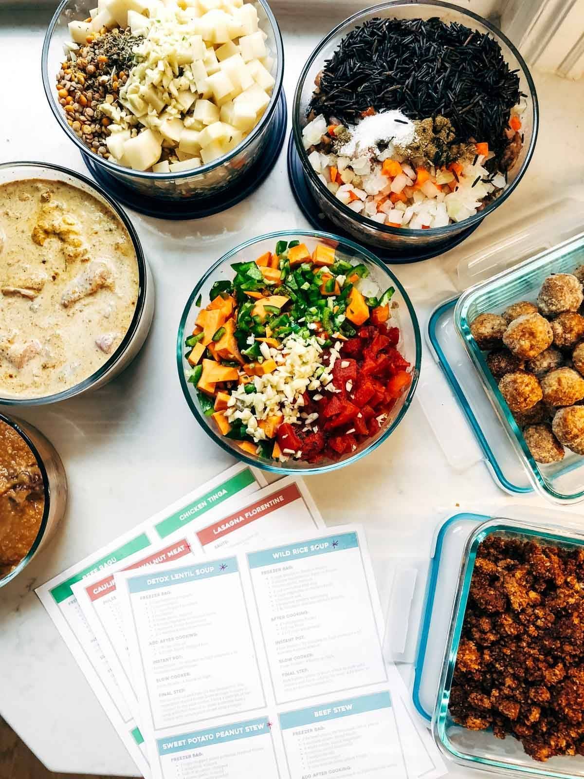 Print outs of freezer meal instructions surrounded by freezer meals in various glass containers.