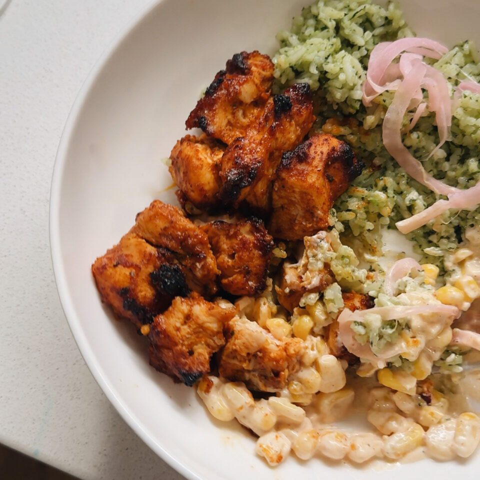 Chicken, corn, and rice in a bowl with pickled onions.